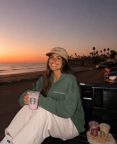 Woman wearing Thank You For Staying oversized zip hoodie at a California beach sunset